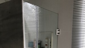 A bathroom with a glass shower enclosure, white tiled walls, and a small shelf with toiletries. - Near Praia do Forte - second block (Cabo Frio)