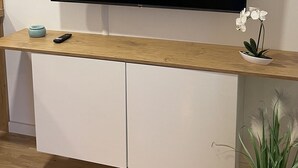 A flat-screen TV mounted on a wall above a wooden console with a remote and a small plant.