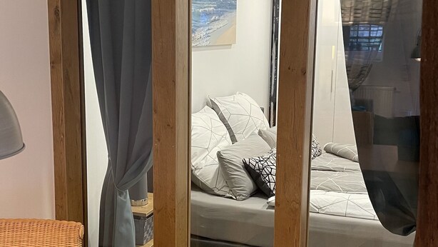 A bedroom with a bed, a window with curtains, a bedside table, and a chair.