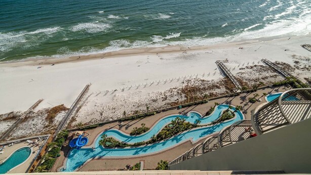 An aerial view of a resort with a beach, a swimming pool, and a lifeguard tower. - New to the Rental Market!  Lazy River and Water Slide! (Orange Beach)