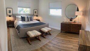 Un dormitorio con cama, mesitas de noche, cómoda, espejo y ventana.