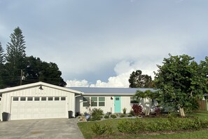 A single-story house with a garage, a turquoise door, and a small garden with various plants.