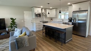 Una cocina moderna con armarios blancos, electrodomésticos de acero inoxidable y una isla central con taburetes de bar.
