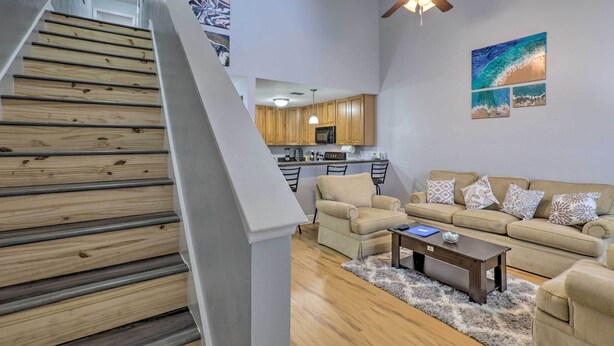 A modern living room with a staircase, a ceiling fan, and a kitchen in the background. - Tidy Tallahassee Townhome ~ 7 Mi to Downtown! (Tallahassee)