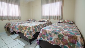 A hotel room with two single beds, each with a patterned bedspread and matching pillows. The room has plain walls and a tiled floor. - Apê no melhor de LagoaNova Por Carpediem (Natal)