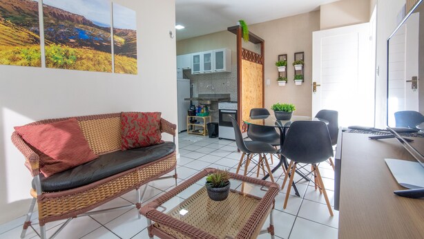 A modern living room with a sofa, a coffee table, and a dining area with chairs and a table. - Apê no melhor de LagoaNova Por Carpediem (Natal)