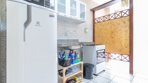 A compact kitchen with a refrigerator, microwave, and stove. There are shelves with various items and a trash bin. - Apê no melhor de LagoaNova Por Carpediem (Natal)