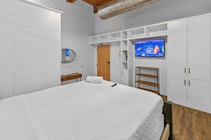 A bedroom with a large bed, a TV mounted on the wall, a wooden door, and white cabinetry.