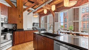 A modern kitchen with wooden cabinets, stainless steel appliances, and large windows with shutters. - Luxe Loft Downtown (Indianapolis)