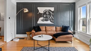 Moderni olohuone, jossa on tumma seinä, ruskea nahkasohva, pyöreä sohvapöytä ja lattiavalaisin.