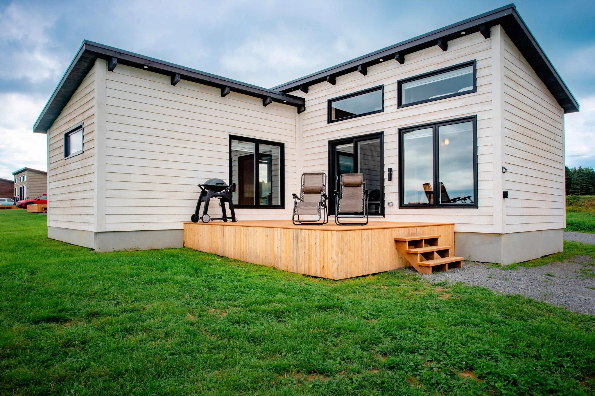 A modern two-story house with a covered patio area, large windows, and a grill.