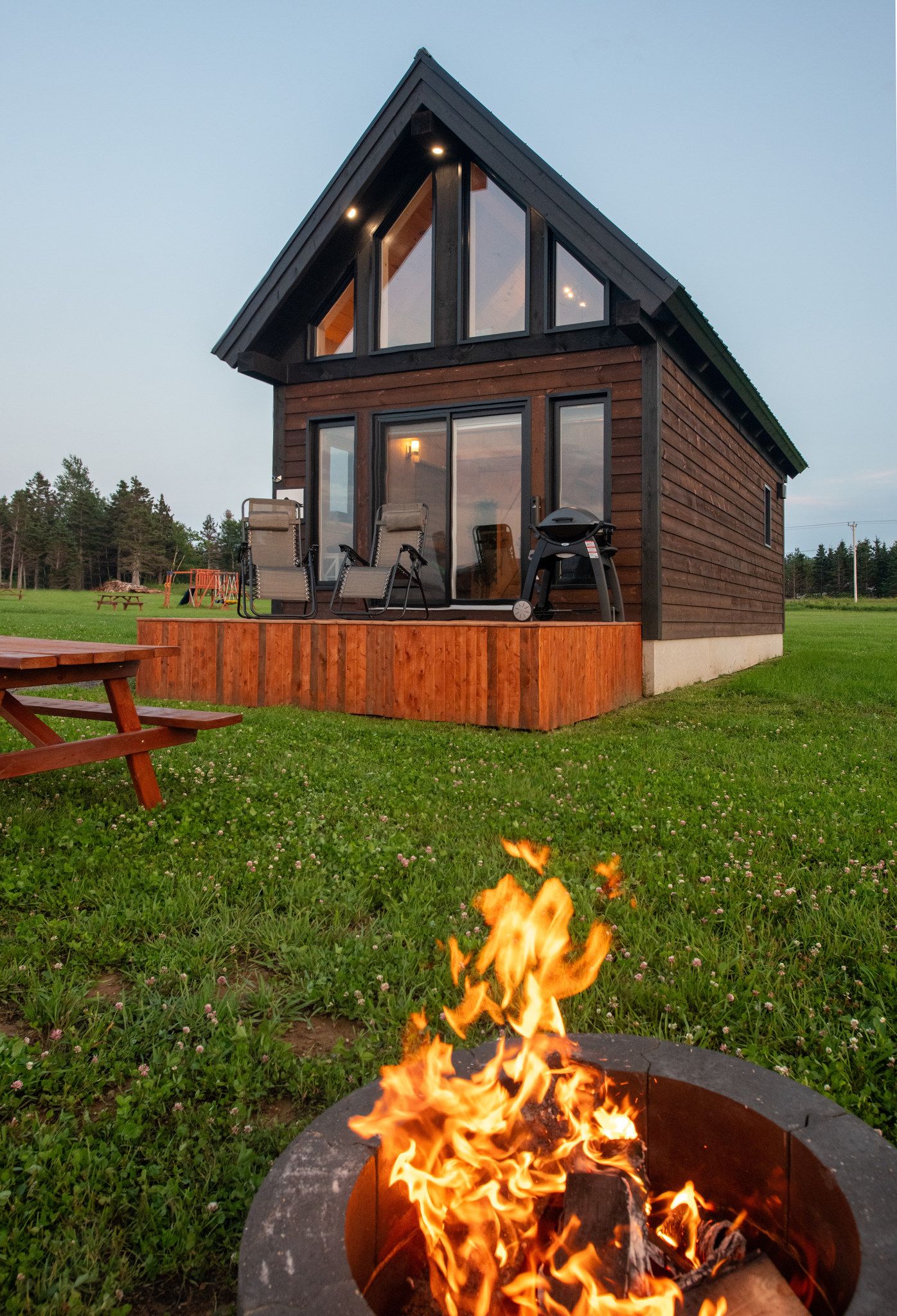 Una cabaña de madera con una terraza, un brasero y una mesa de picnic.