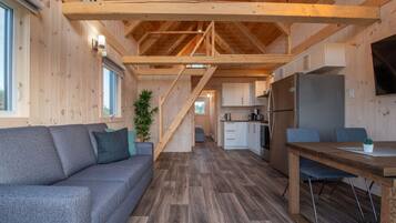 A modern log cabin interior with a sofa, dining table, kitchen, and staircase.