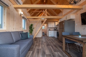 A modern log cabin interior with a sofa, dining table, kitchen, and staircase. - Chalets Nautika (Gaspé)