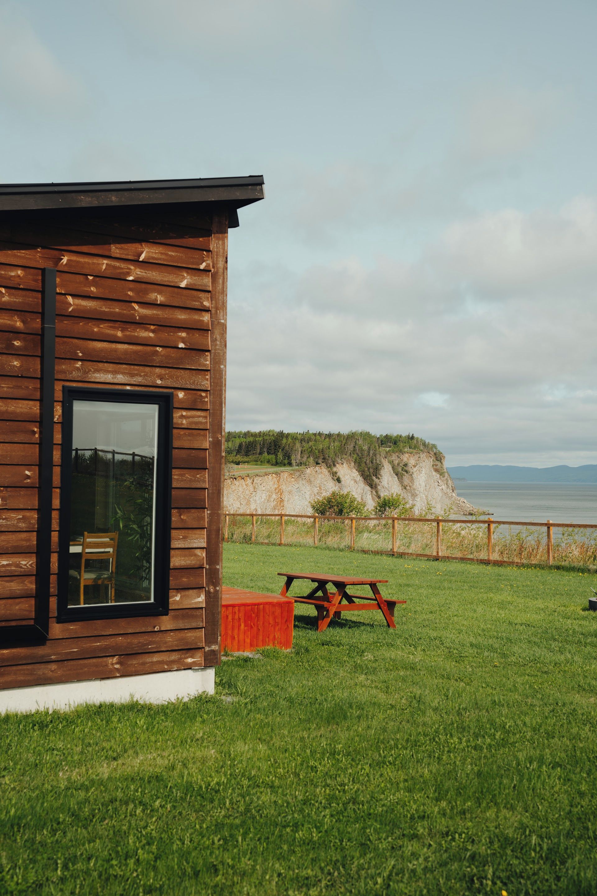 Une cabane en bois avec une grande fenêtre, une table de pique-nique et une cour gazonnée.