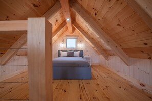 A bedroom with a sloped ceiling, wooden walls, a bed, and a window. - Chalets Nautika (Gaspé)