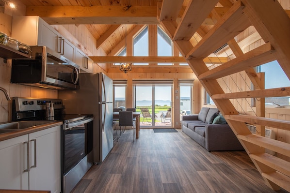 A modern kitchen with stainless steel appliances, a dining area with a view, and a cozy seating area. - Chalets Nautika (Gaspé)