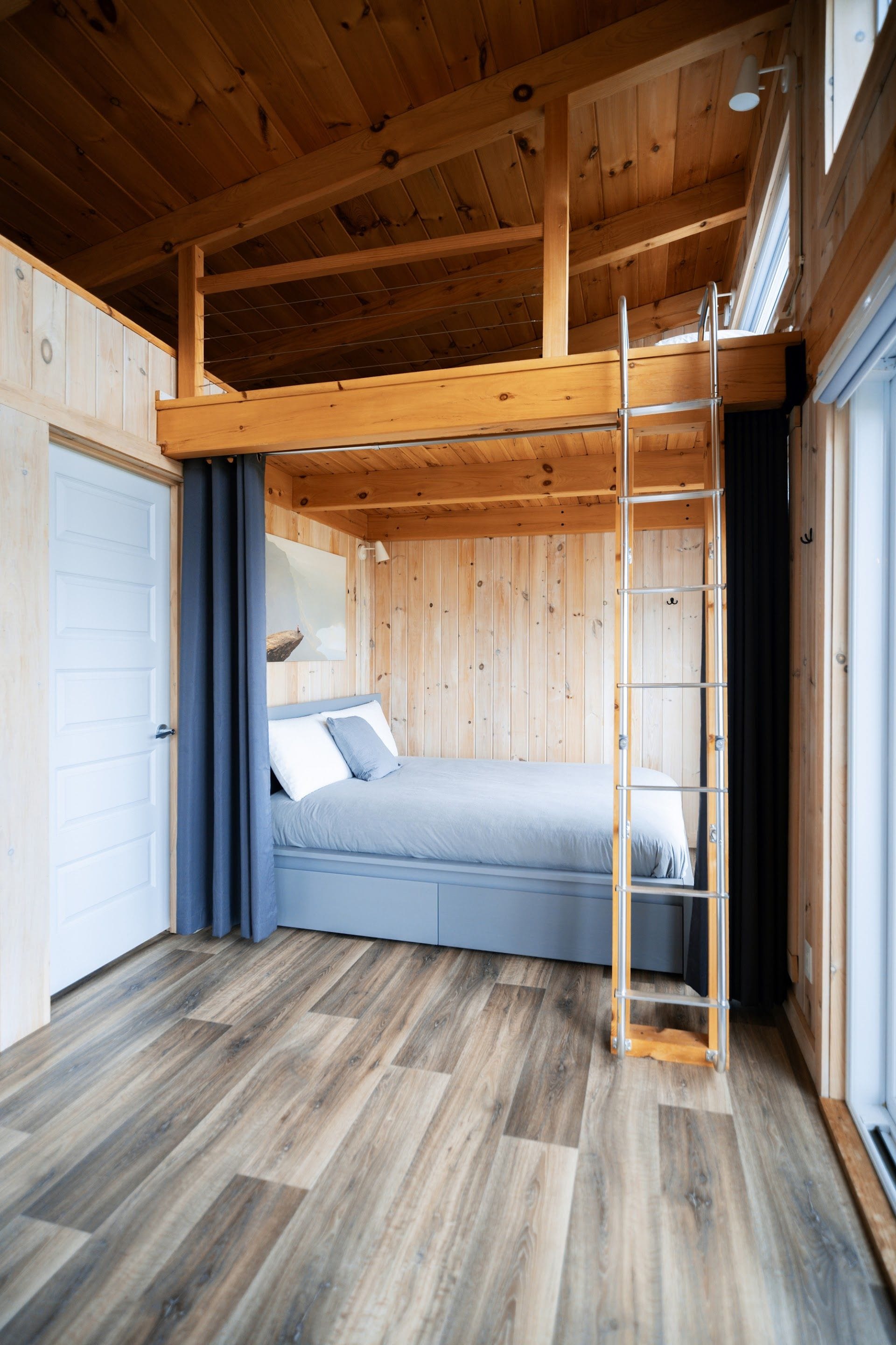 Une chambre à coucher de taille réduite, avec un lit superposé, une échelle et une grande fenêtre.