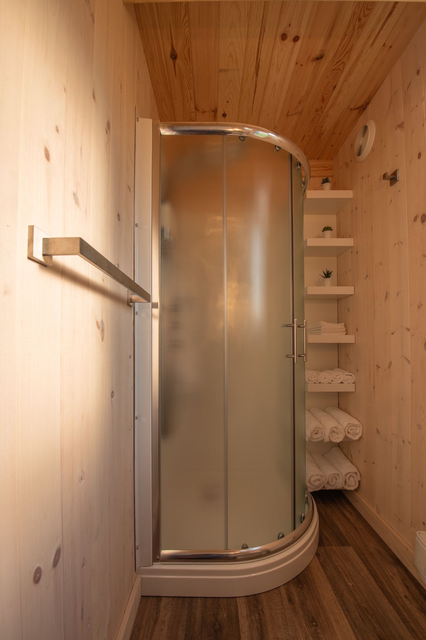 A shower enclosure with a glass door, wooden walls, and a shelf with towels.