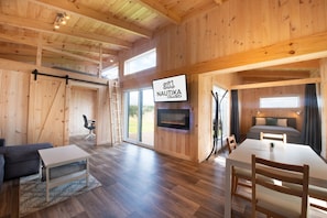 Un interior de madera con un comedor, un sofá, un televisor montado en la pared y una chimenea.