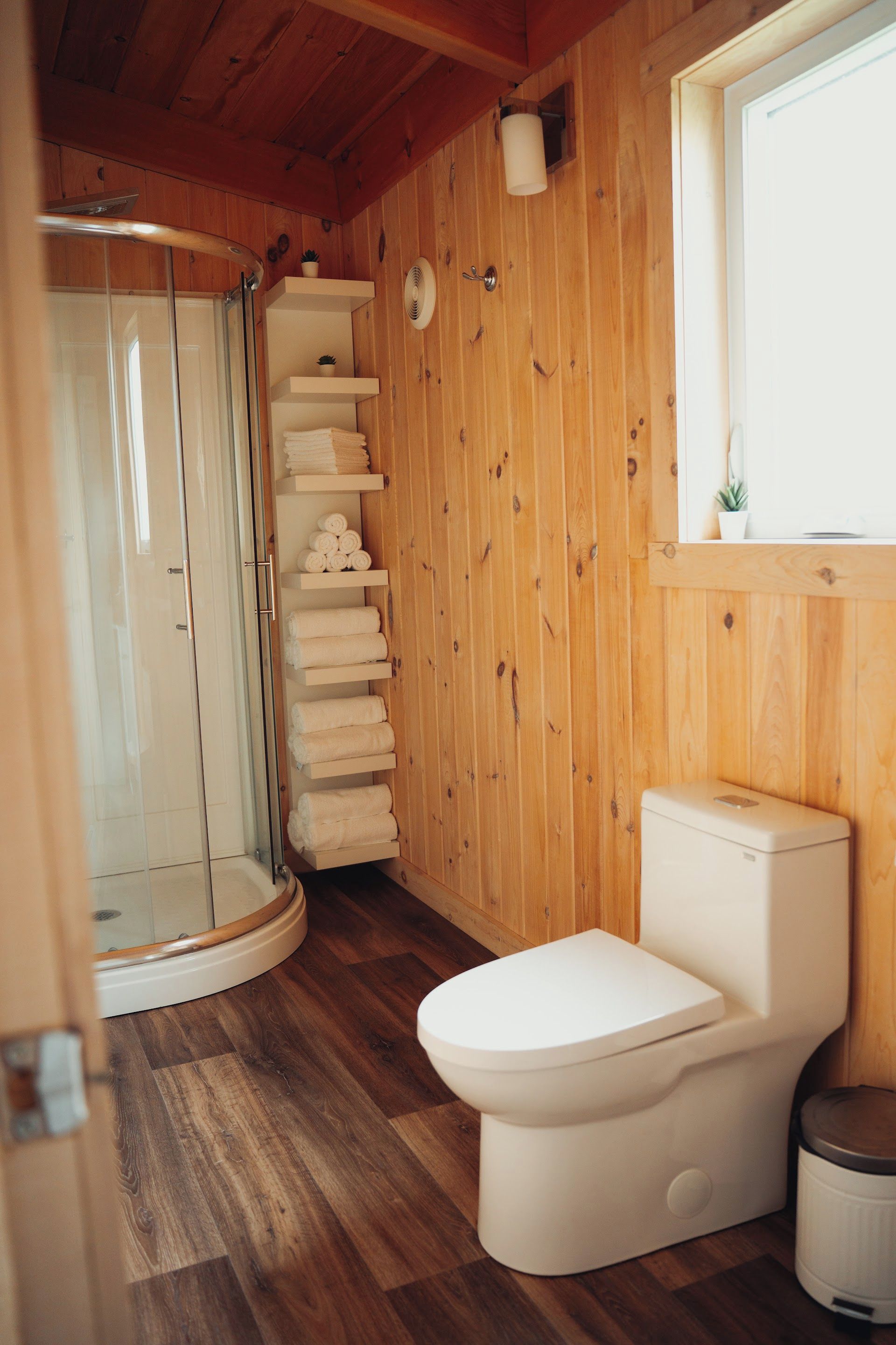 Un interior de madera con cabina de ducha de vidrio, inodoro y ventana.