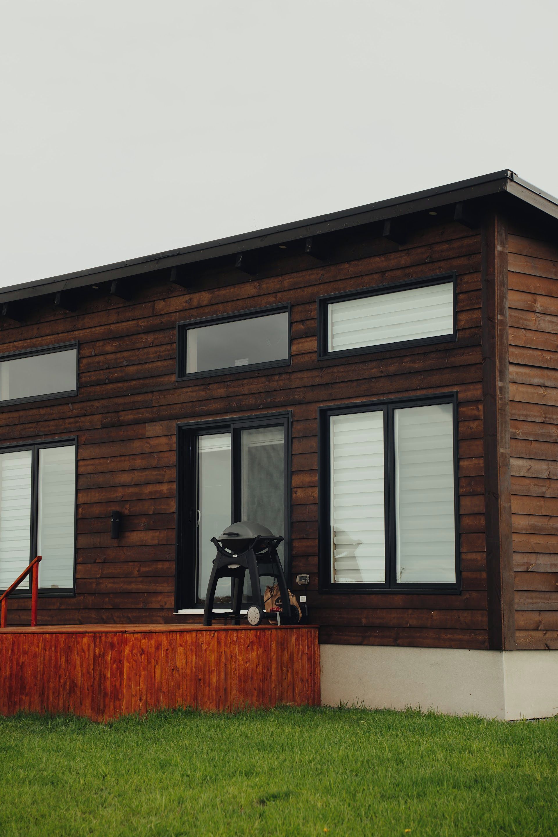 Una casa moderna de dos pisos con fachada de madera, ventanas grandes y un porche cubierto.