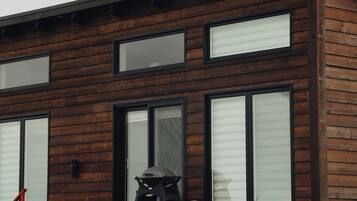 Una casa moderna de dos pisos con fachada de madera, ventanas grandes y un porche cubierto.