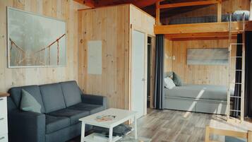 A cozy cabin interior with a sofa, a small table, a bunk bed, and a ladder.