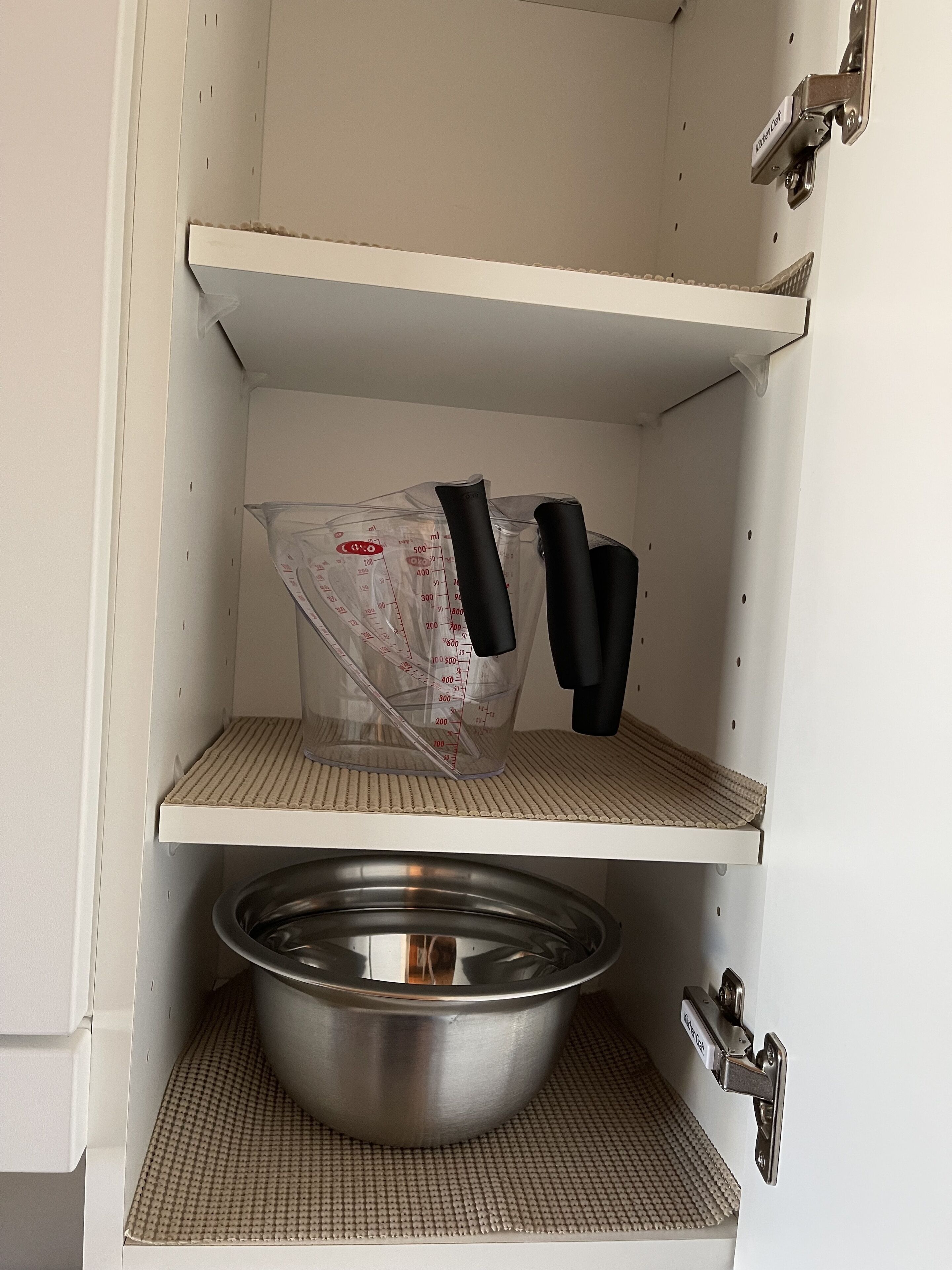 A kitchen with a stainless steel pot on the bottom shelf and a measuring cup on the top shelf.