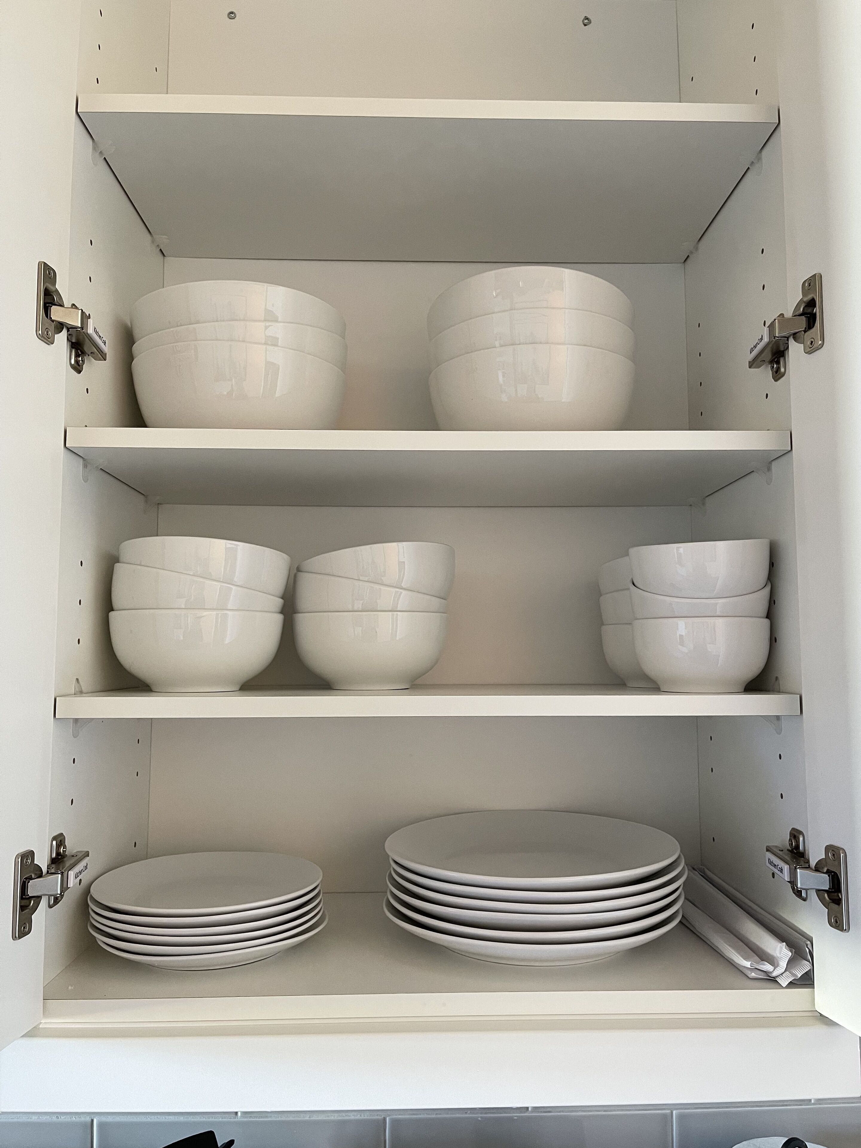 Een keukenkast met drie plateaus, elk gevuld met witte kommen en borden.