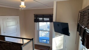 A room with a window, a ceiling fan, a door, and a TV mounted on the wall.