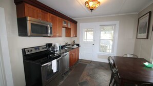 A kitchen with wooden cabinets, a stainless steel microwave, a black stove, and a dining table with chairs.