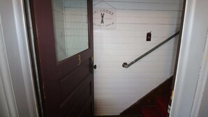 A wooden staircase with a metal handrail and a door with a number plate.