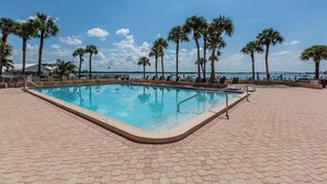Una piscina rettangolare con bordo piastrellato, circondata da palme e sedie a sdraio, con vista sull'oceano e un ponte sullo sfondo.