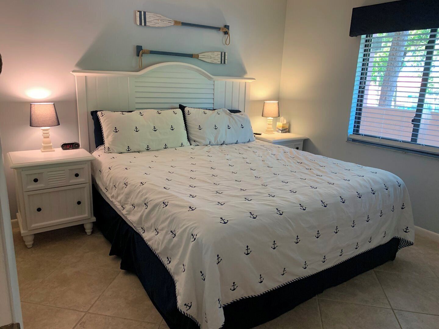 A bedroom with a bed, two bedside tables, a nightstand, and a window with blinds.