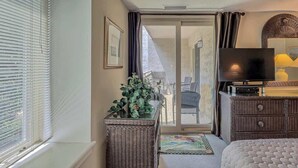 Ein Hotelzimmer mit Bett, Fernseher, einem Korbtisch mit Pflanze und einer Schiebetür zum Balkon.