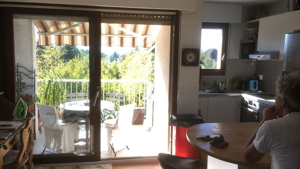 Eine moderne Küche mit Essbereich, einer Schiebetür zu einem Balkon und Blick auf Grünfläche.