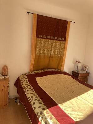 A bedroom with a bed, a nightstand, a wooden dresser, and a window with curtains.