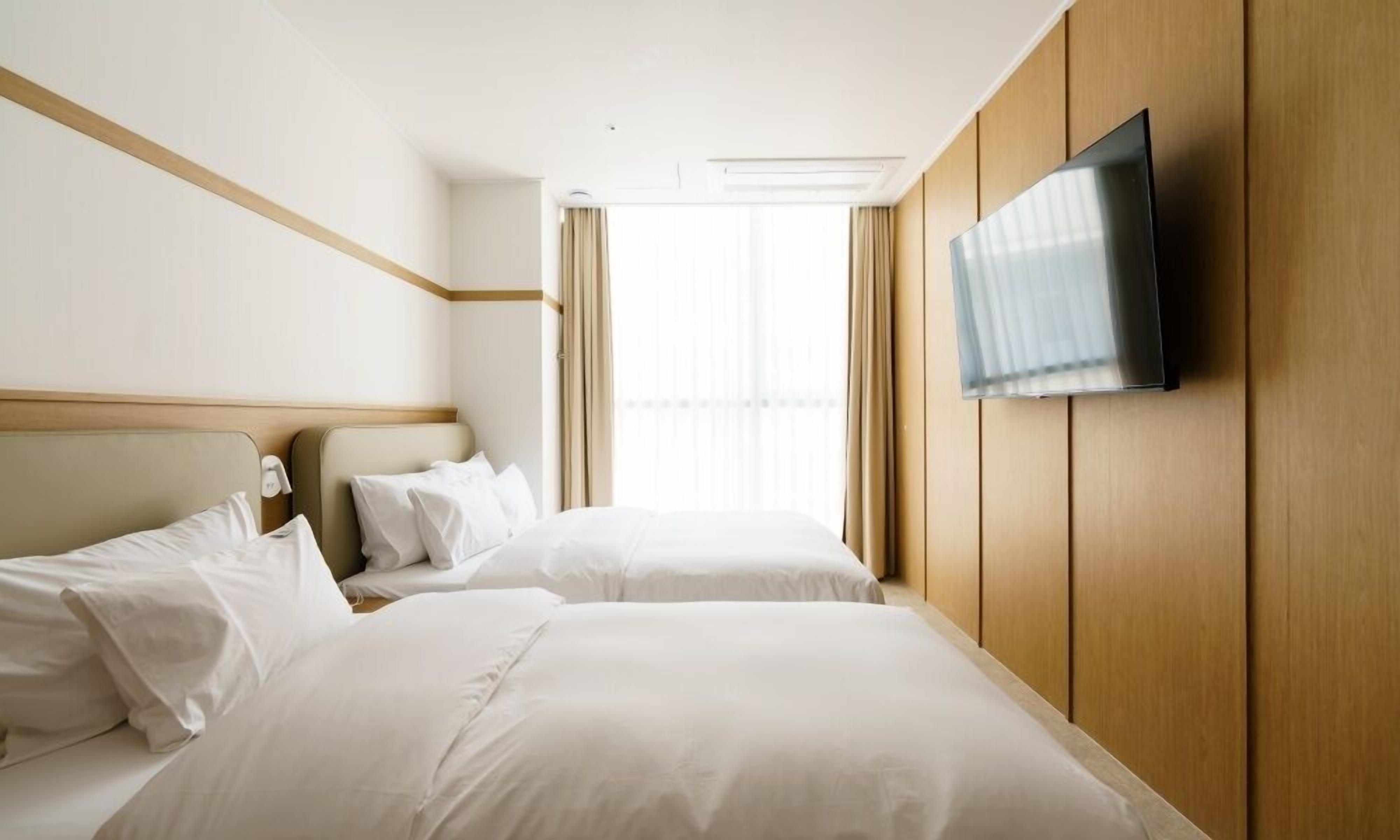 A hotel room with two beds, a flat-screen TV mounted on the wall, and a large window with curtains.