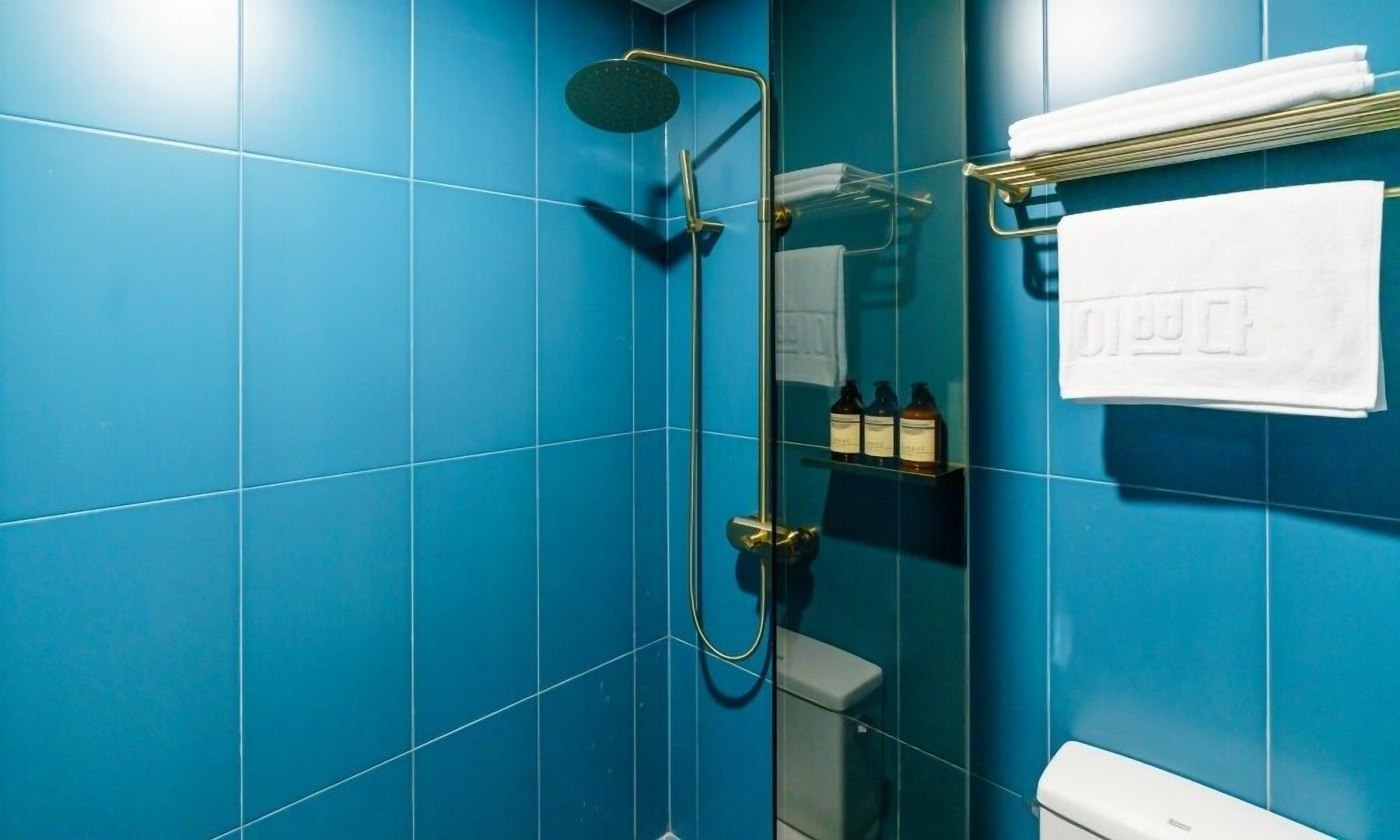 A bathroom with blue tiles, a glass shower enclosure, a toilet, and a towel rack with folded towels.