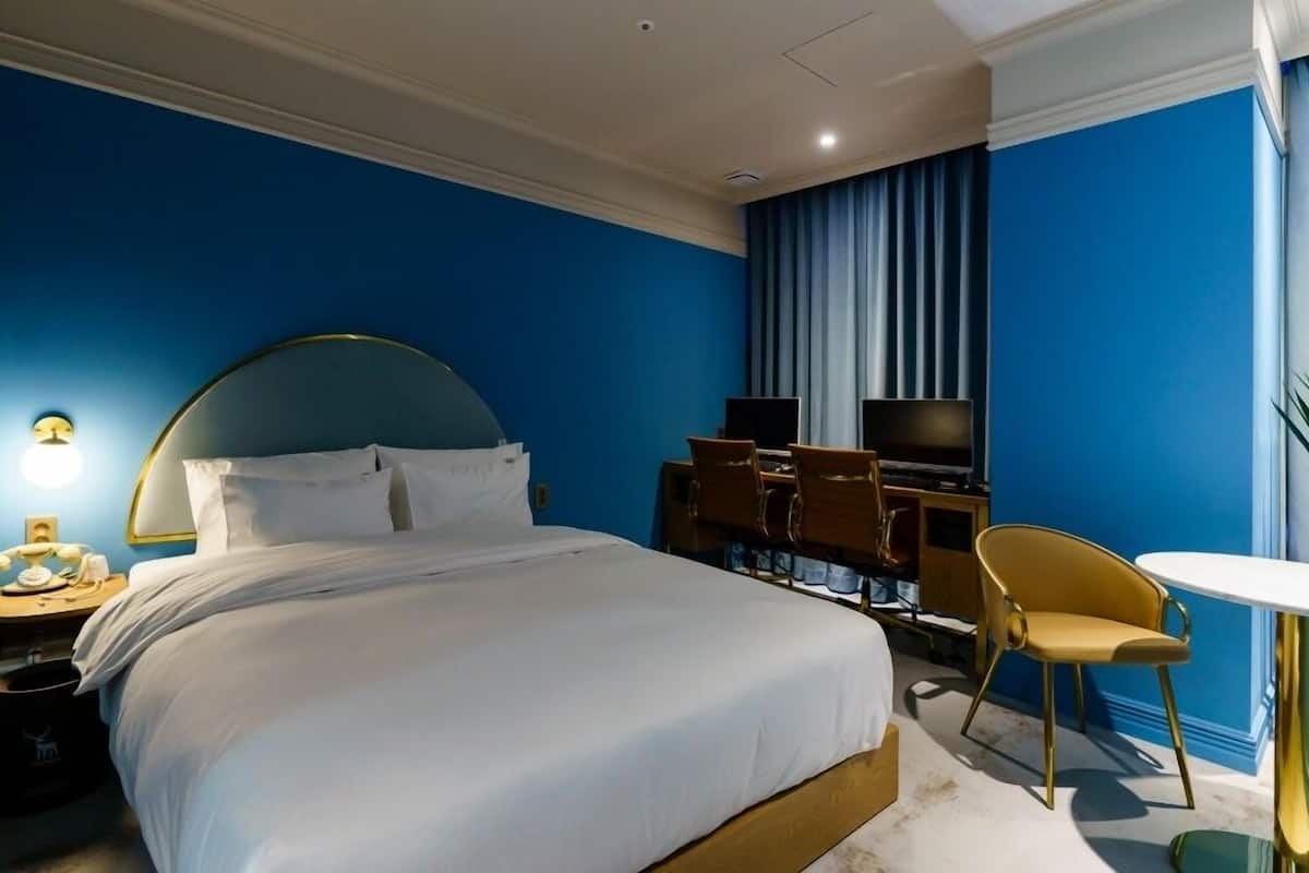 Habitación de hotel con una cama grande, un escritorio con dos monitores, una silla y una mesita.