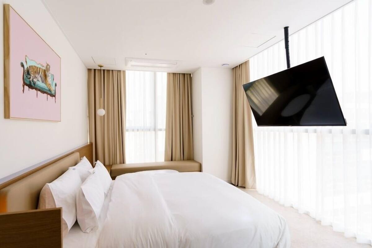 Una habitación de hotel con cama, televisor montado en la pared y ventana con cortinas.