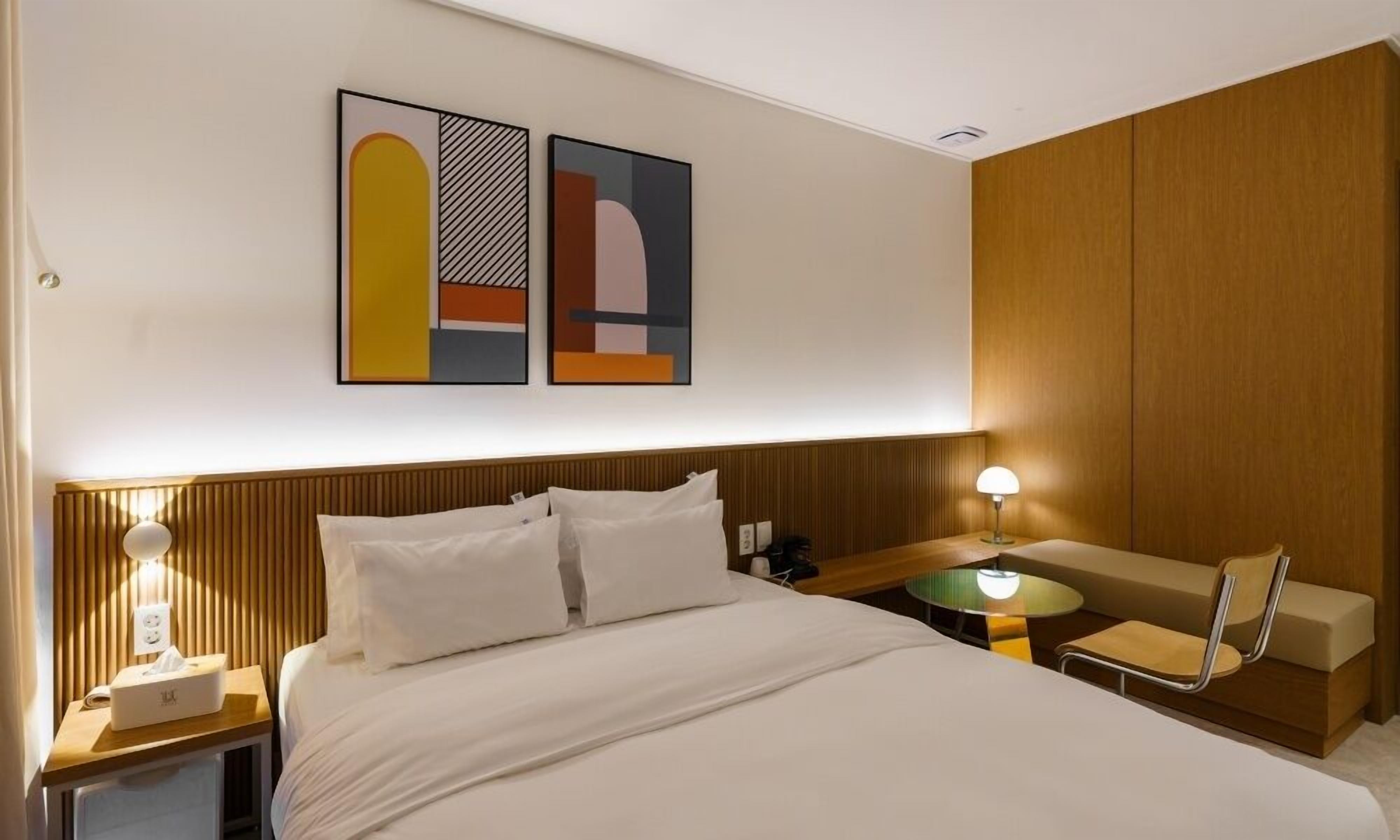 Habitación de hotel con cama, mesita de noche, lámpara y una pequeña mesa con una silla.