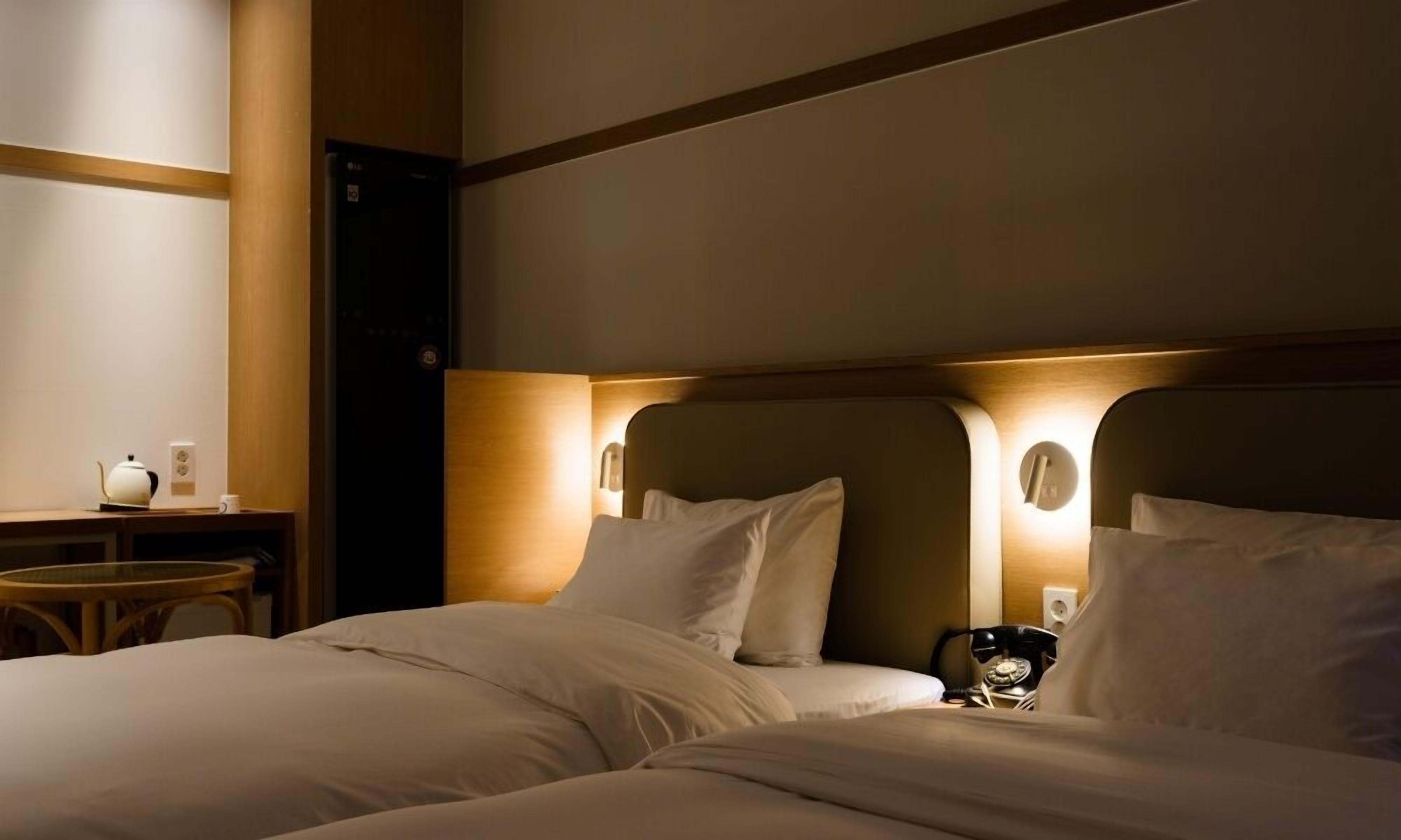 Una habitación de hotel con dos camas, una mesita de noche con lámpara y un teléfono.