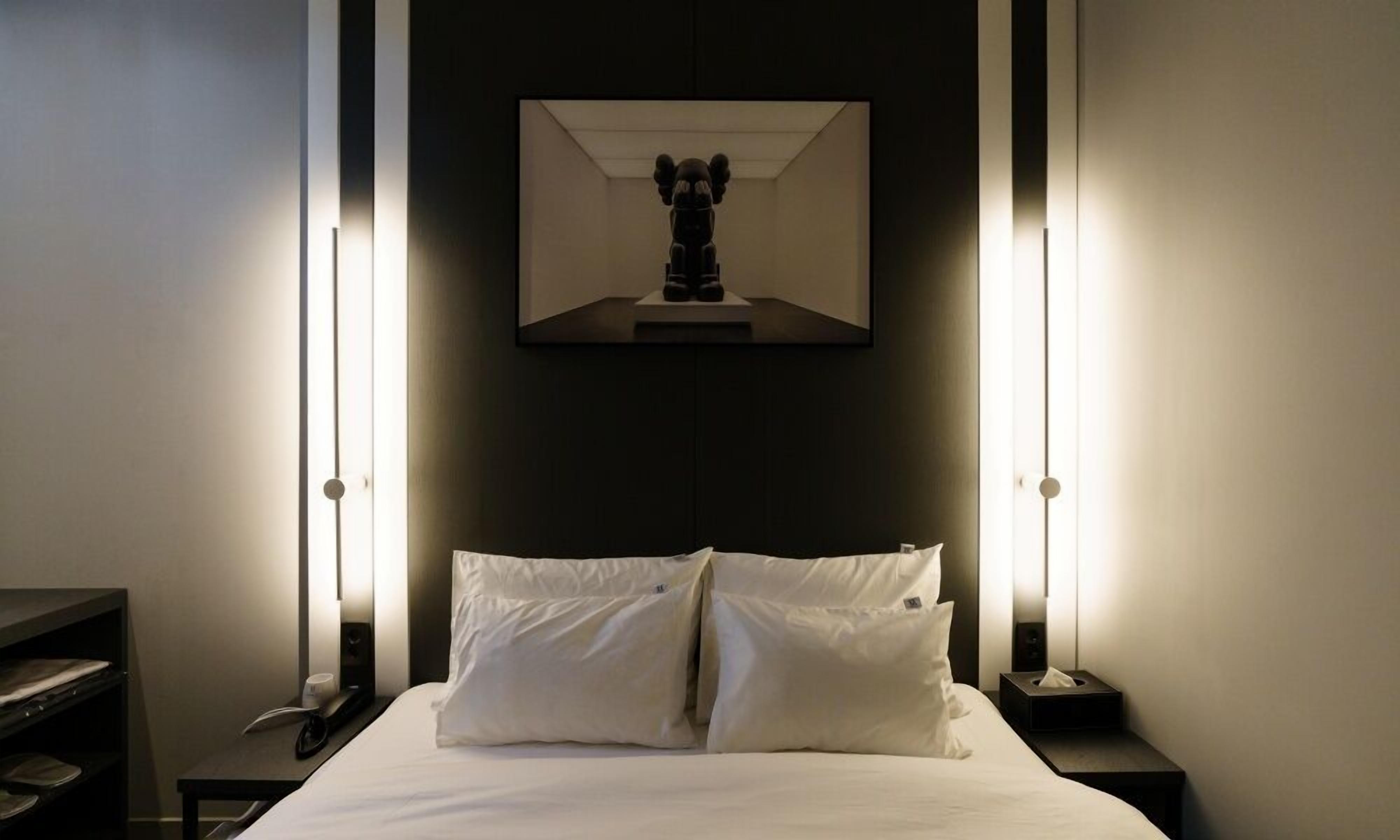 Ein Hotelzimmer mit einem Bett, zwei Nachttischen, einer Wandleuchte und einem gerahmten Bild über dem Bett.