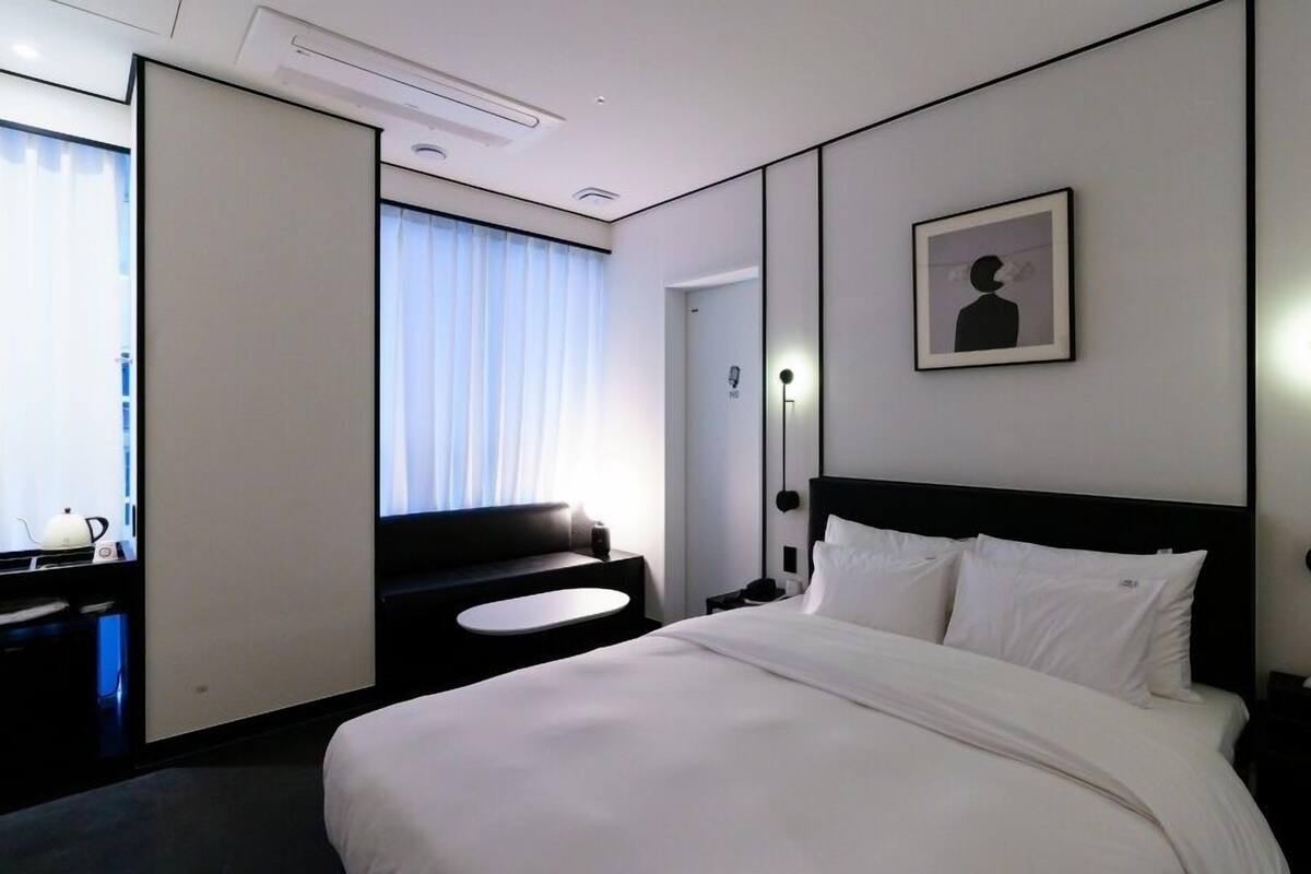 Una habitación de hotel con una cama grande, un escritorio con silla, un sofá pequeño, una mesita de noche y una lámpara de pie. También hay un cuadro en la pared.
