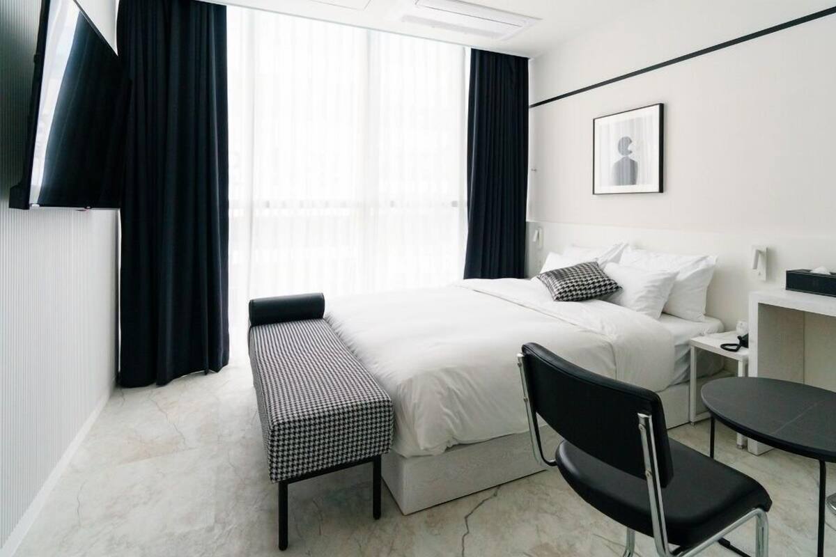 Una habitación de hotel con cama, escritorio, silla, una mesita y televisor en la pared.