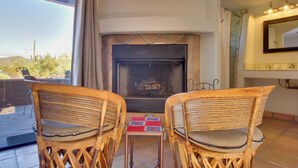 A cozy seating area with two wicker chairs and a small table, a fireplace, and a large window with a view of the desert. - 'La Paloma' - Full Circle Ranch Studio w/ Views! (Cave Creek)