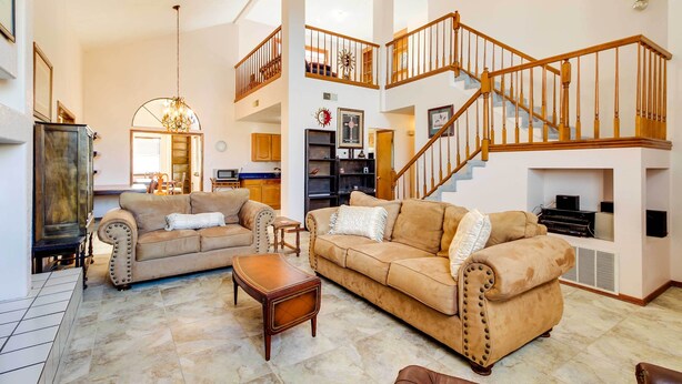 A spacious living room with a high ceiling, a staircase, and a fireplace.