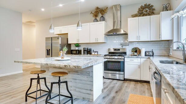 A modern kitchen with white cabinets, a large island with stools, stainless steel appliances, and pendant lighting. - Stunning Clovis Home ~ 1 Mile to Old Town! (Clovis)